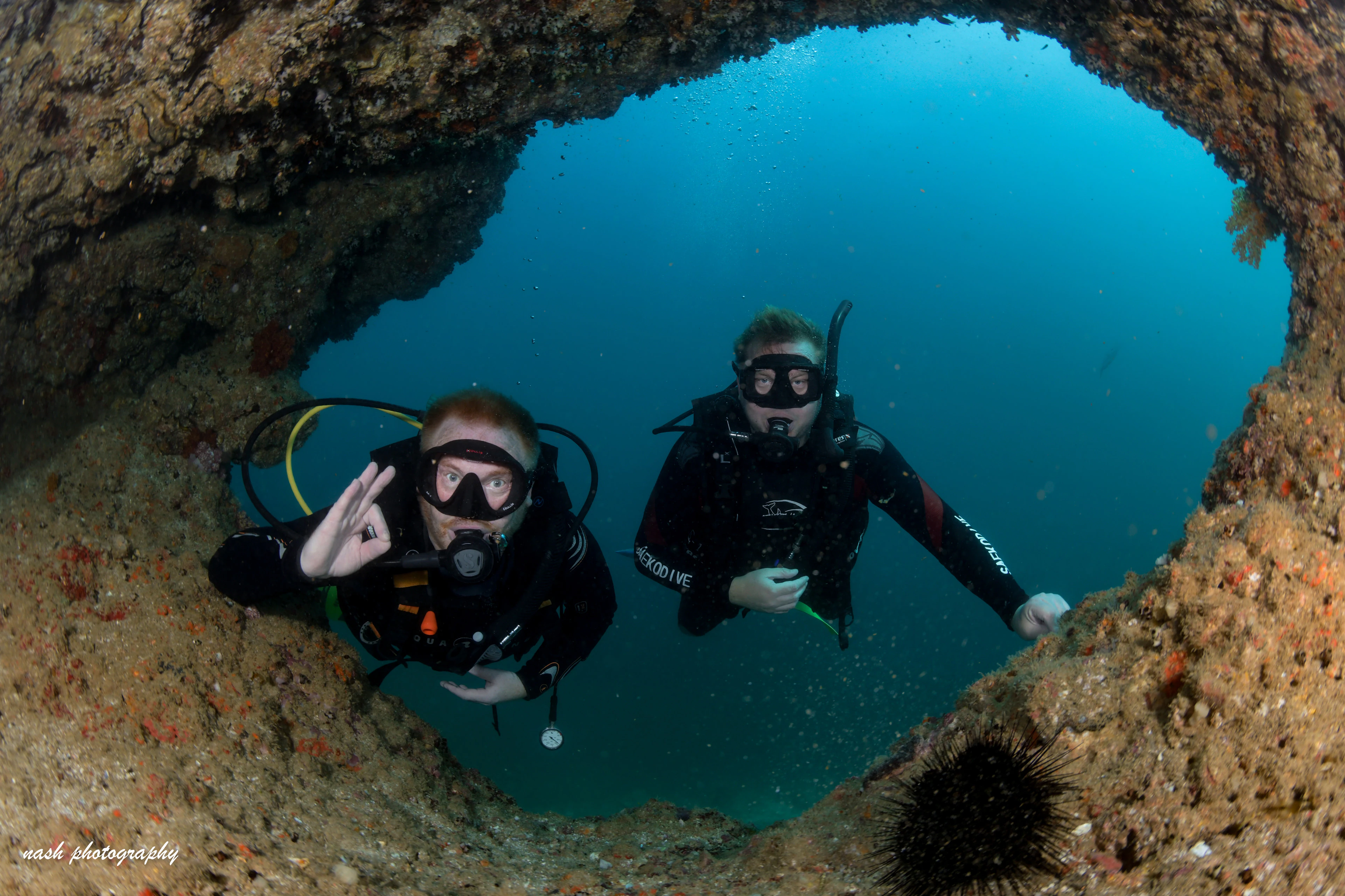 Two new divers giving the OK sign in a reef arch